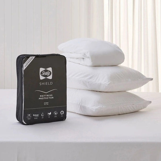 Mattress protector packaging with stacked pillows on a bed