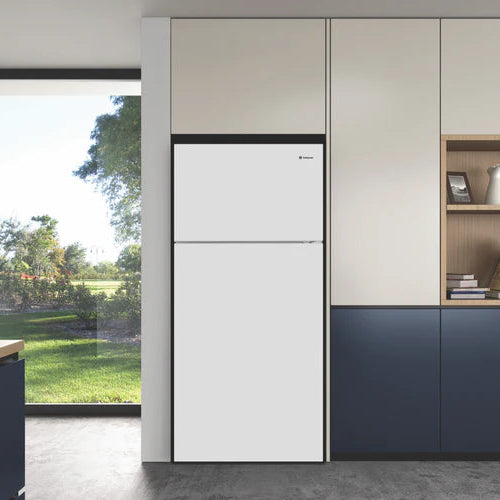 Modern kitchen with white refrigerator, blue cabinets, and a view of greenery outside.