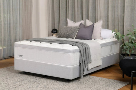 Gray mattress with white bedding and decorative pillows in a bedroom setting.