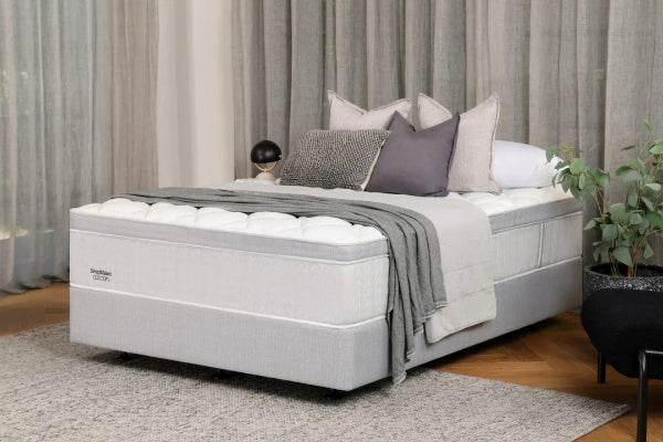 Gray mattress with white bedding and decorative pillows in a bedroom setting.