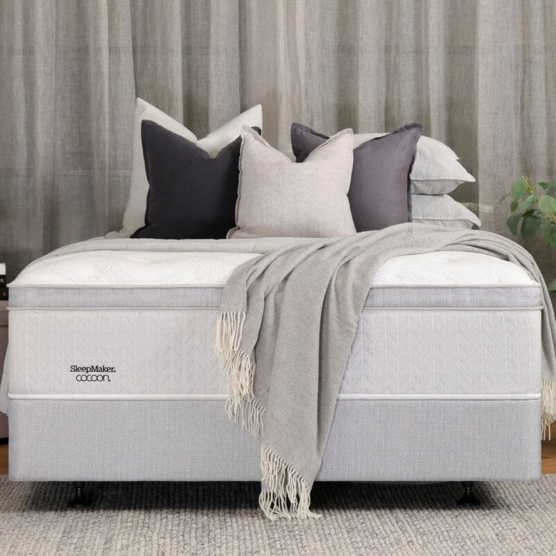 Gray mattress with decorative pillows and a blanket in a bedroom setting.