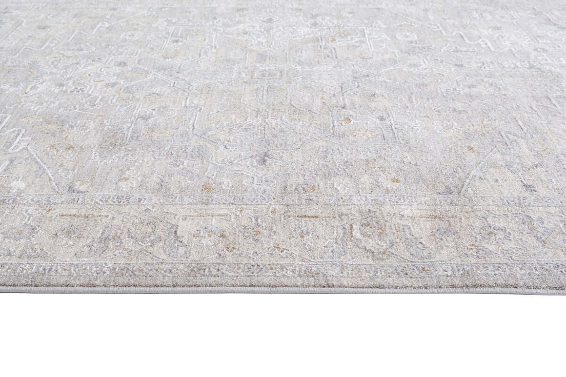A close-up view of a light beige and gray area rug with a distressed, faded traditional pattern.