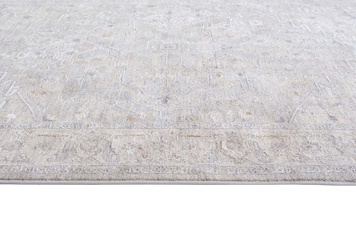 A close-up view of a light beige and gray area rug with a distressed, faded traditional pattern.