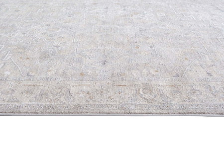 A close-up view of a light beige and gray area rug with a distressed, faded traditional pattern.