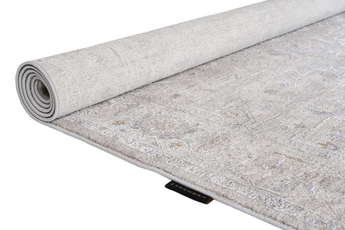 A light gray and beige patterned area rug, partially rolled up to show both its top surface and underside, photographed on a clean white background.