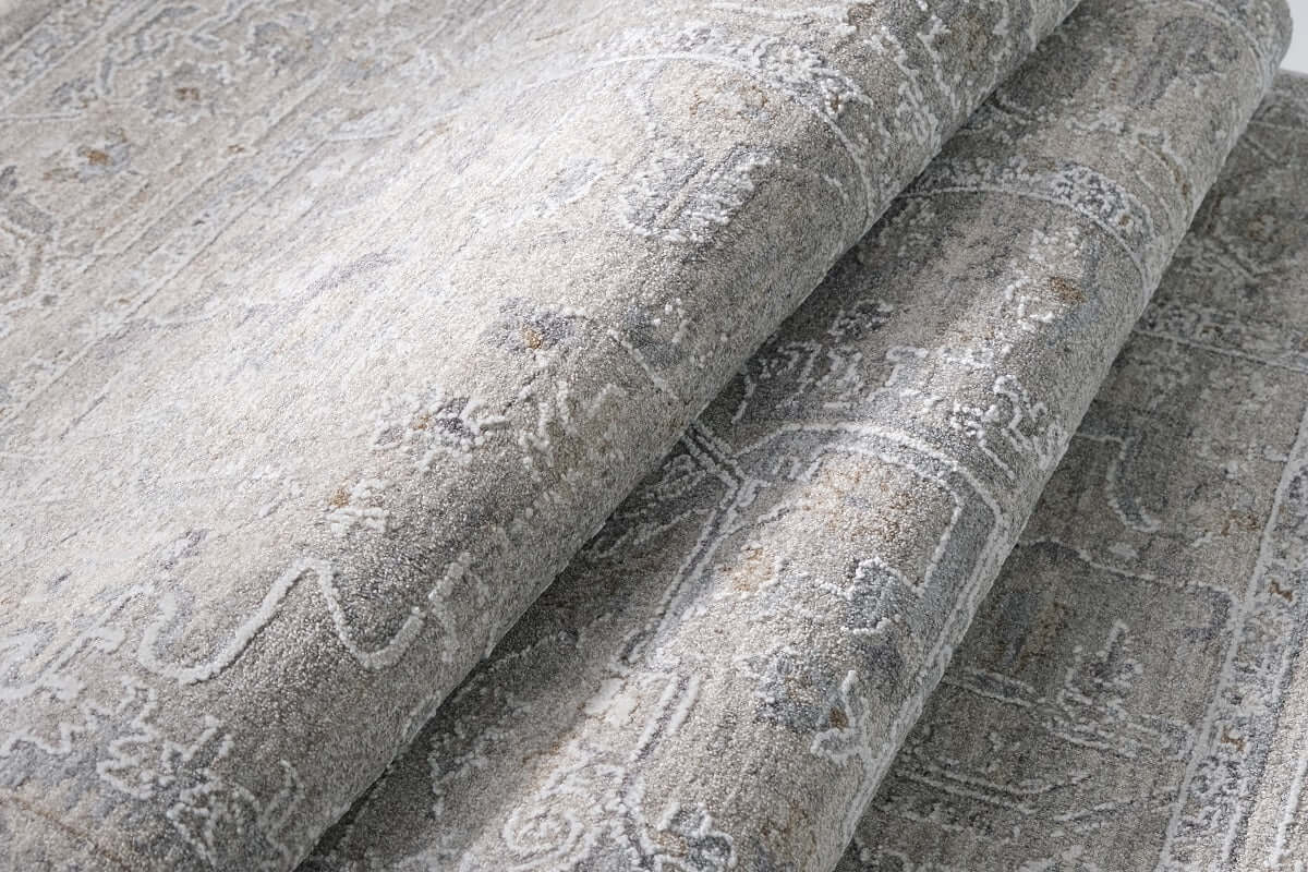 A close-up of a folded area rug with a distressed, traditional pattern in shades of gray, beige, and off-white.