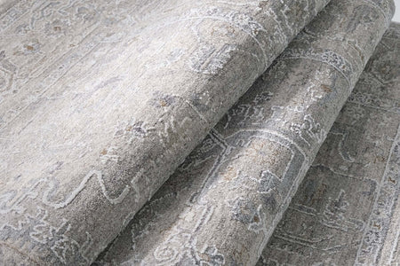 A close-up of a folded area rug with a distressed, traditional pattern in shades of gray, beige, and off-white.