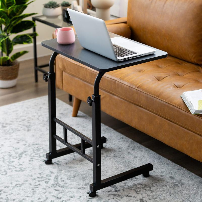 Laptop on a portable desk next to a brown leather sofa in a living room.
