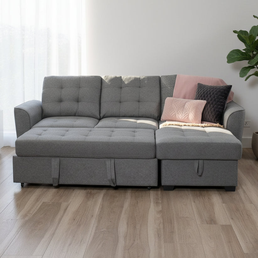 Gray sectional sofa with cushions in a room with large windows and a view of trees.