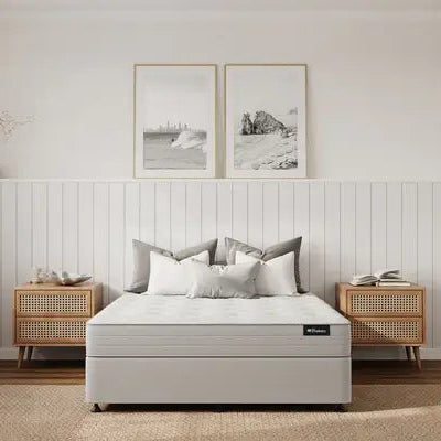 White mattress in a bedroom with wooden nightstands and framed pictures on the wall.