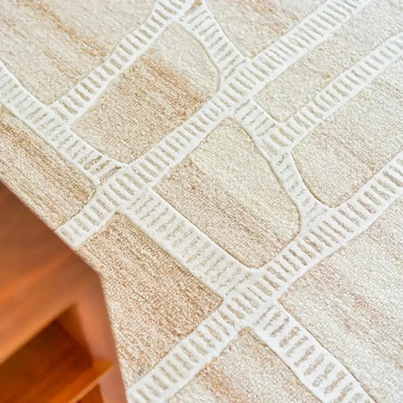 Close-up of a textured beige and white patterned tablecloth on a wooden surface.