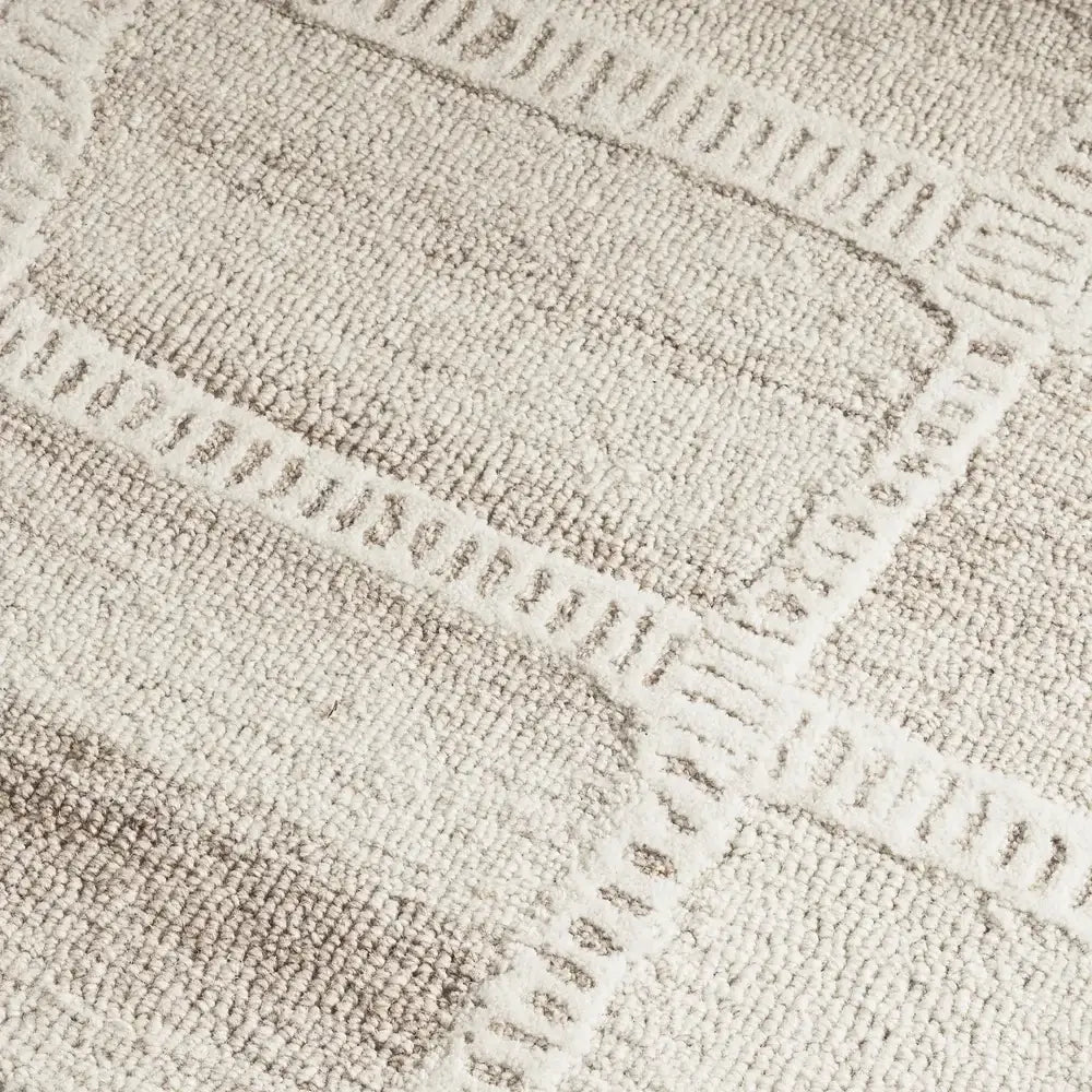 Close-up of a textured area rug with a geometric pattern in warm beige and cream tones.