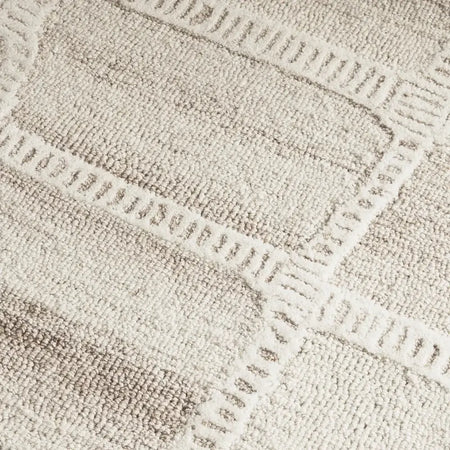 Close-up of a textured area rug with a geometric pattern in warm beige and cream tones.